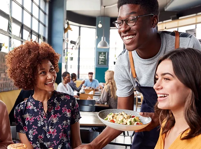 Fröhliche Mitarbeitende beim Mittagessen, werden gerade vom Kellner serviert